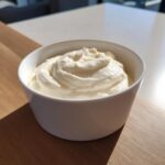 A close-up of thick, creamy homemade alfredo sauce swirled in a small white ramekin.