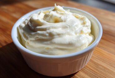 A close-up of thick, creamy homemade alfredo sauce swirled high in a small white ramekin on a wooden surface.