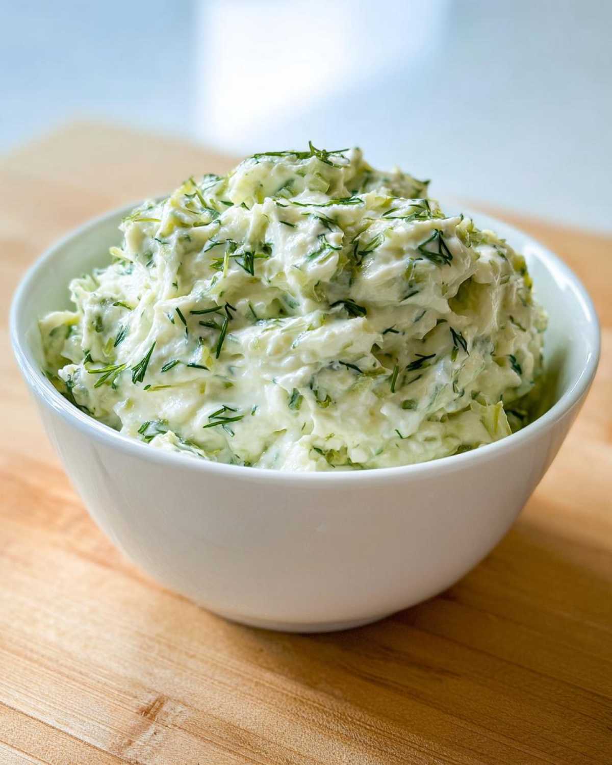 A white bowl filled high with creamy, chunky pickle dip garnished generously with fresh dill.