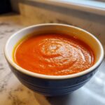 Close-up of a vibrant orange bowl filled with creamy roasted tomato soup.