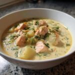 Close-up of a bowl of creamy salmon soup filled with chunks of pink salmon, potatoes, and fresh dill.