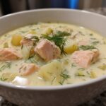 Close-up of a bowl of creamy salmon soup featuring chunks of pink salmon, potatoes, and fresh dill.