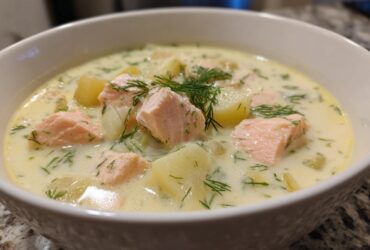 Close-up of a bowl of creamy salmon soup featuring chunks of pink salmon, potatoes, and fresh dill.