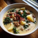 A close-up of a creamy bowl of Zuppa Toscana soup featuring sausage, potatoes, kale, and crumbled bacon.