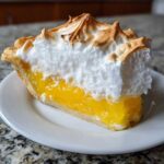 A perfect slice of lemon meringue pie showing bright yellow filling and tall, toasted meringue.
