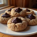 Five classic peanut butter blossom cookies, rolled in sugar and topped with a chocolate kiss, arranged on a white plate.