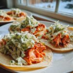 Close-up of three delicious salmon tacos filled with flaked salmon and topped with creamy green slaw.
