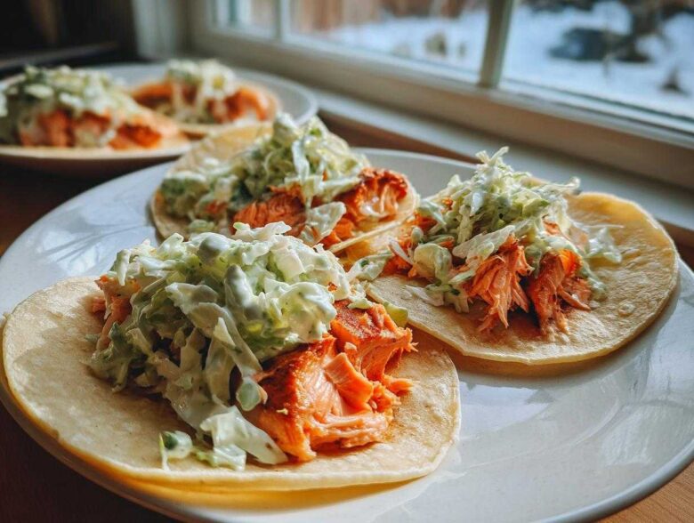 Close-up of three delicious salmon tacos filled with flaked salmon and topped with creamy green slaw.