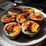 Seven pieces of freshly sliced tuna kimbap arranged on a white plate, showing bright orange tuna filling and yellow egg.