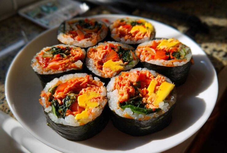 Seven pieces of freshly sliced tuna kimbap arranged on a white plate, showing bright orange tuna filling and yellow egg.