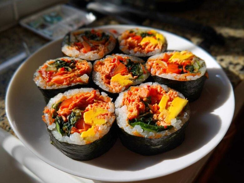 Seven pieces of freshly sliced tuna kimbap arranged on a white plate, showing bright orange tuna filling and yellow egg.