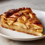 Close-up of a perfectly baked slice of apple tart showing caramelized apples and a lattice crust.