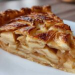 Close-up of a thick slice of golden brown apple tart showing flaky crust and layered cinnamon-spiced apples.