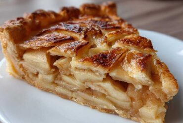 Close-up of a thick slice of golden brown apple tart showing flaky crust and layered cinnamon-spiced apples.