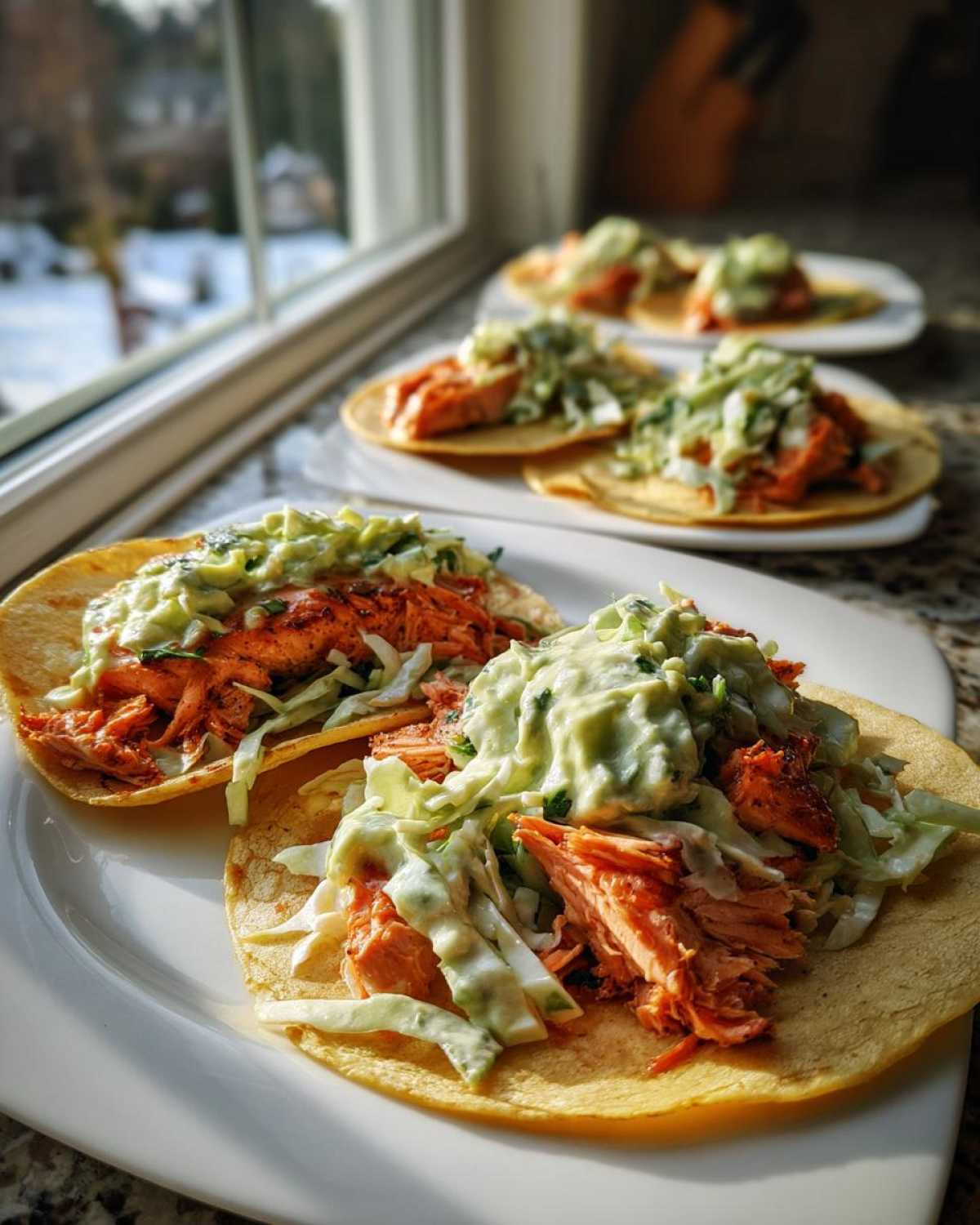 Two beautifully assembled salmon tacos topped with shredded cabbage slaw and creamy avocado sauce, ready to eat.