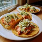 Three delicious salmon tacos filled with flaky orange salmon and topped with creamy green coleslaw on a white plate.