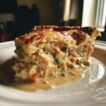 A generous slice of creamy turkey pot pie with flaky crust overflowing onto a white plate.