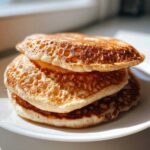Close-up of a stack of three fluffy discard pancakes with golden-brown, bubbly surfaces.