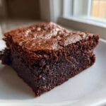 Close-up of a single, rich, fudgy slice of vegan date brownies on a white plate.