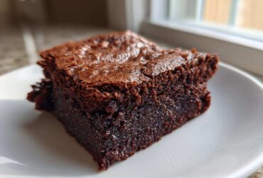 Close-up of a single, rich, fudgy slice of vegan date brownies on a white plate.