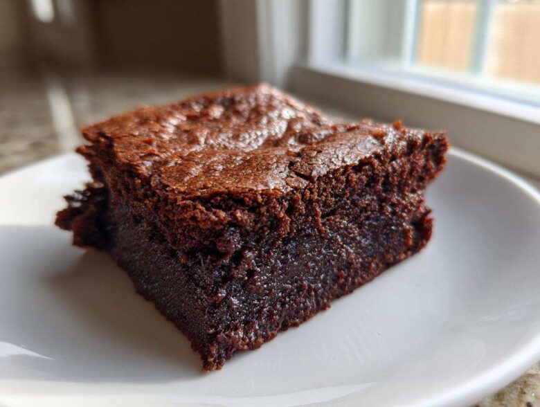 Close-up of a single, rich, fudgy slice of vegan date brownies on a white plate.