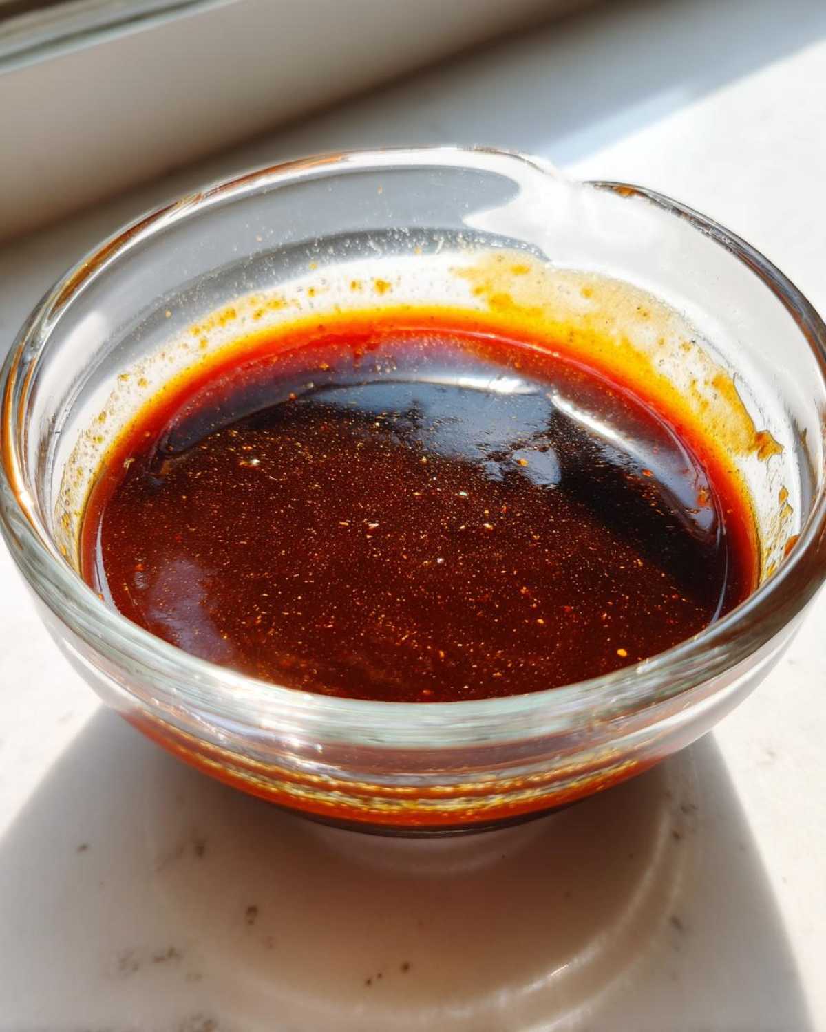 Close-up of thick, dark homemade teriyaki sauce glistening in a small clear glass bowl.