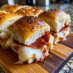 Close-up of gooey, cheesy pizza sliders filled with pepperoni on a wooden board.