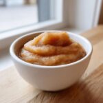 A close-up of homemade applesauce, lightly dusted with cinnamon, served in a white bowl.