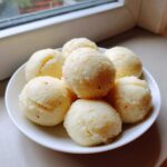 A white bowl filled with several perfectly rounded balls of light yellow fufu, resting near a window.