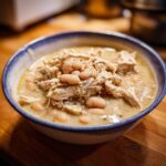 A close-up bowl filled with creamy instant pot white chicken chili, topped with shredded chicken and white beans.