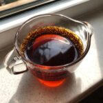 A glass measuring cup filled with dark, rich homemade teriyaki sauce, sitting on a counter near a window.