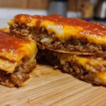 Cross-section view of a homemade Mexican pizza showing layers of seasoned ground beef, melted cheese, and red sauce.