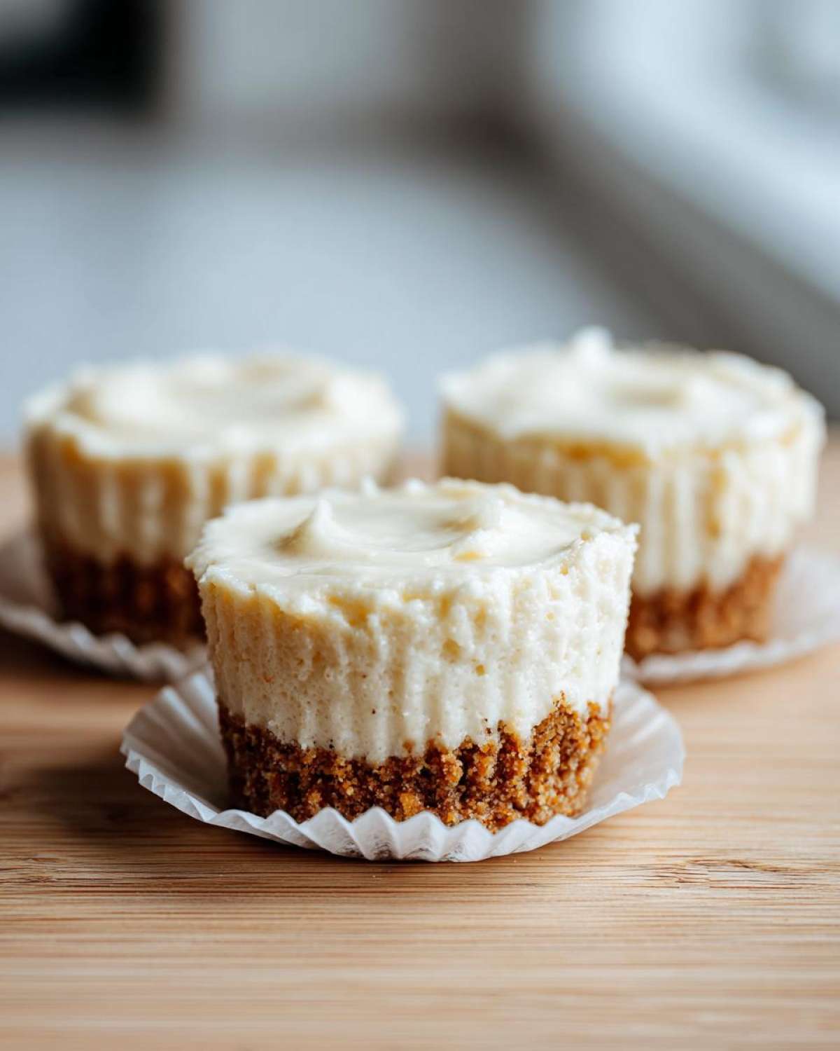 A close-up of a single mini cheesecake with a graham cracker crust, sitting in a paper liner.