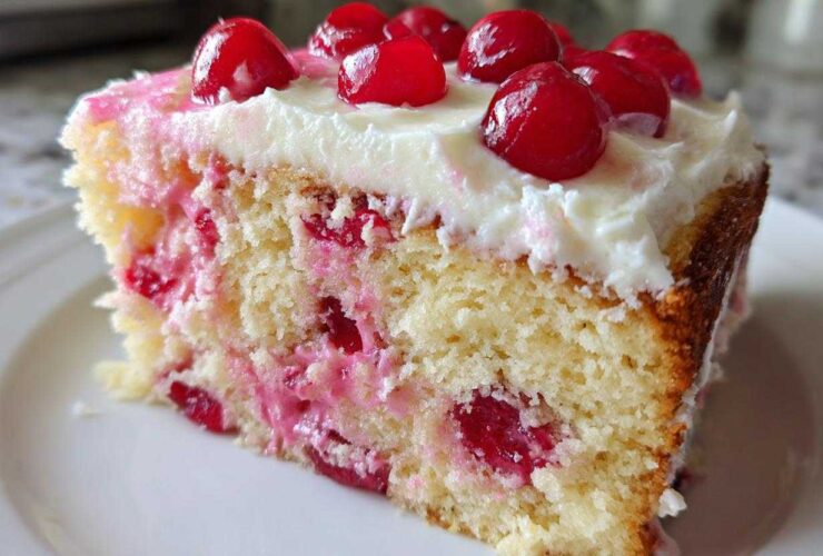 Close-up of a moist slice of vintage cherry cake, featuring a light yellow crumb studded with bright red cherries and topped with white frosting and whole cherries.