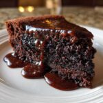 Close-up of a rich, moist slice of chocolate pudding cake topped with glossy, flowing chocolate sauce.