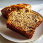 Close-up of a thick slice of moist sugar free banana bread showing walnuts and a rich brown crumb.