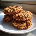 A stack of four hearty, golden-brown breakfast cookie treats made with oats and dried cranberries.