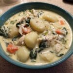 Close-up of a bowl of creamy olive garden chicken gnocchi soup, featuring plump gnocchi, shredded chicken, spinach, and carrots.