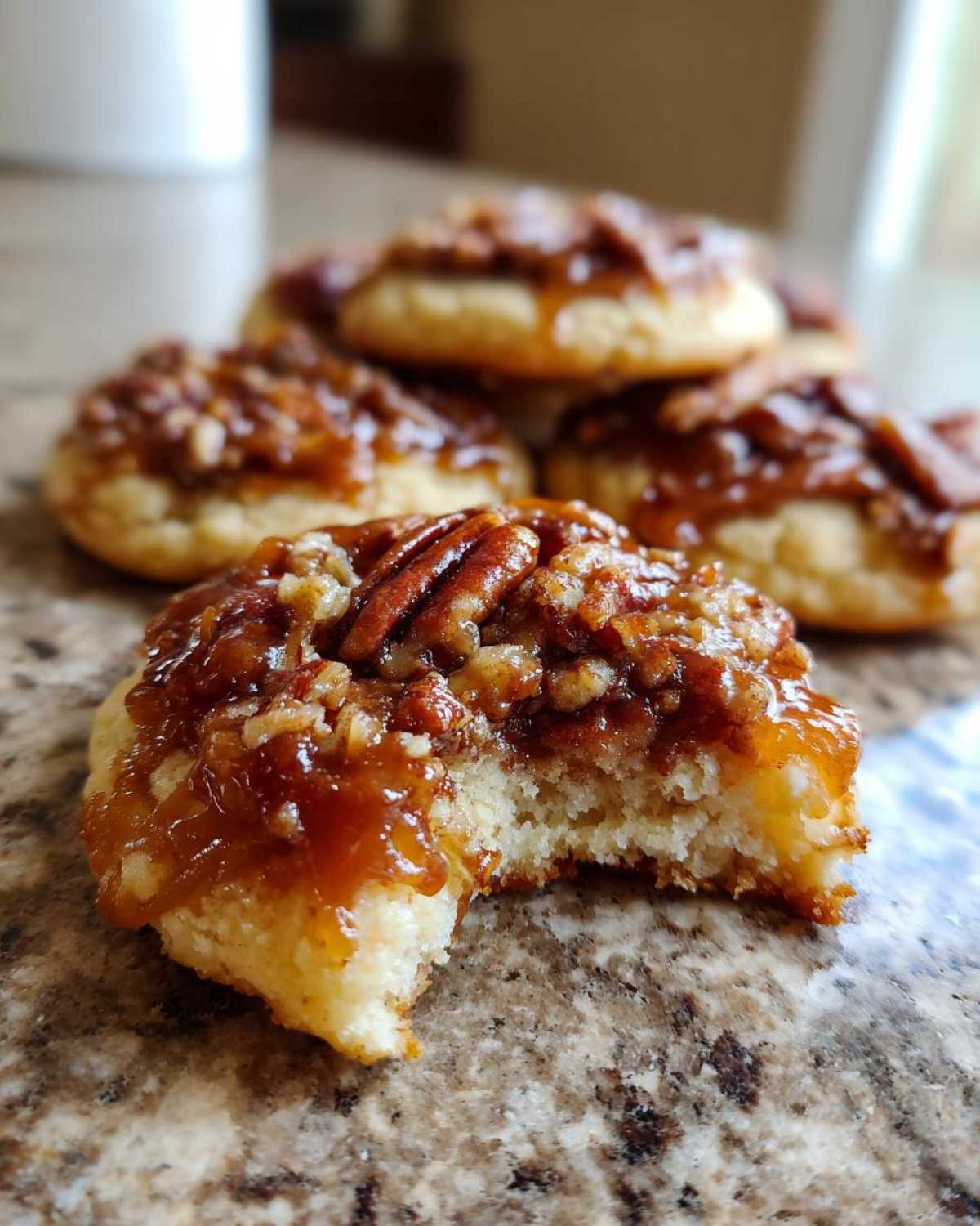 A close-up of a pecan pie cookie with a bite taken out, showing the soft interior and gooey pecan topping.