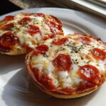 Close-up of two freshly baked pepperoni english muffin pizza halves topped with melted cheese and herbs.