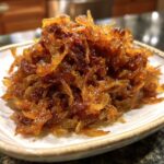 A close-up of a pile of deeply browned and glossy caramelized onions served on a small white dish.