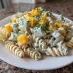Close-up of a serving of creamy pickle pasta salad featuring fusilli pasta, diced pickles, yellow peppers, and fresh dill.
