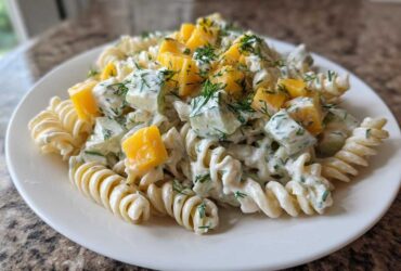 Close-up of a serving of creamy pickle pasta salad featuring fusilli pasta, diced pickles, yellow peppers, and fresh dill.