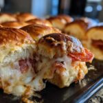 Close-up of a pizza slider pulled apart showing melted, gooey cheese and pepperoni inside the toasted bun.