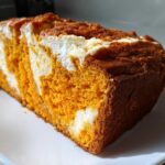 A close-up of a moist slice of pumpkin cream cheese bread showing vibrant orange pumpkin cake swirled with white cream cheese filling.