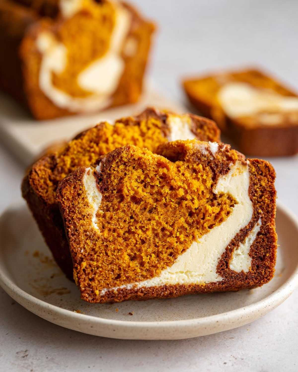 Two thick slices of moist pumpkin cream cheese bread showing the vibrant orange crumb and white cream cheese swirl.
