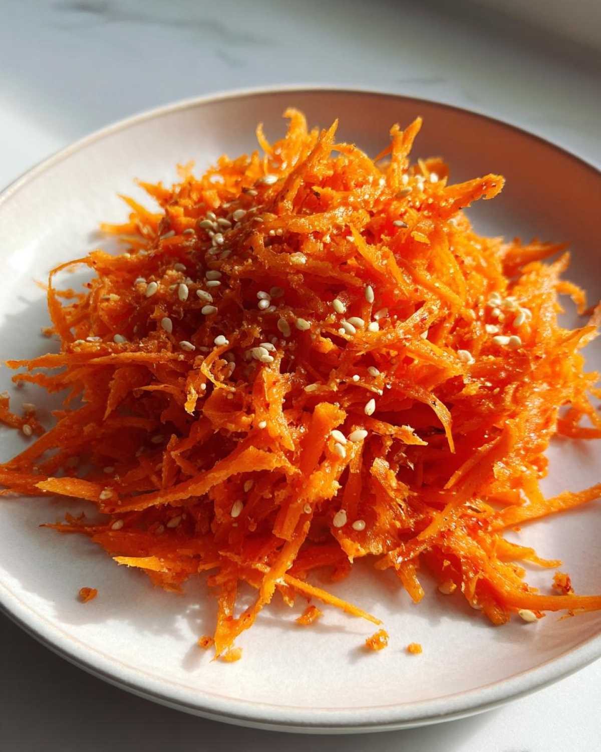 Close-up of a vibrant raw carrot salad made with shredded carrots and sprinkled with white sesame seeds.