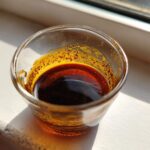 Close-up of rich, dark homemade teriyaki sauce in a small glass cup sitting on a bright windowsill.
