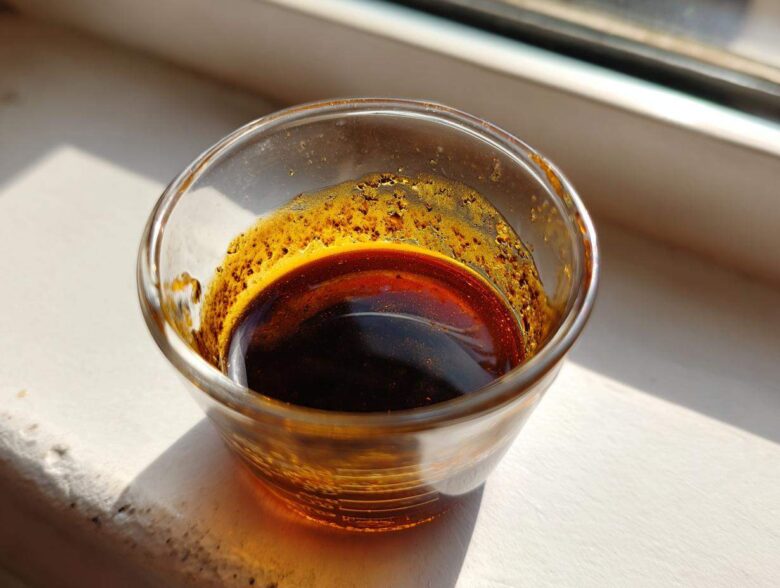Close-up of rich, dark homemade teriyaki sauce in a small glass cup sitting on a bright windowsill.