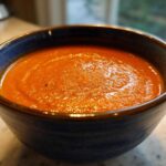 Close-up of a deep blue bowl filled with thick, vibrant orange roasted tomato soup.